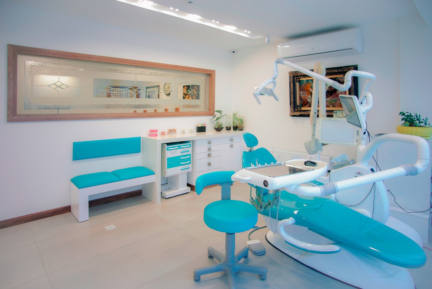 Modern dental clinic with turquoise chair and waiting bench.